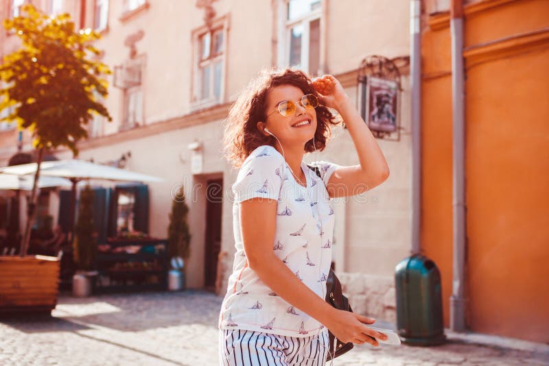 Beautiful young girl using smartphone and listening to the music walking on street. Woman dancing and singing