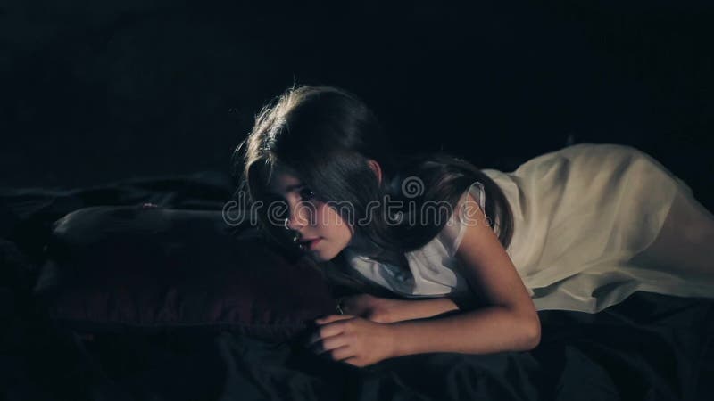 A beautiful young girl wakes up. Dark background. Social project. Long hair. Close-up. white dress. Confused. Happy