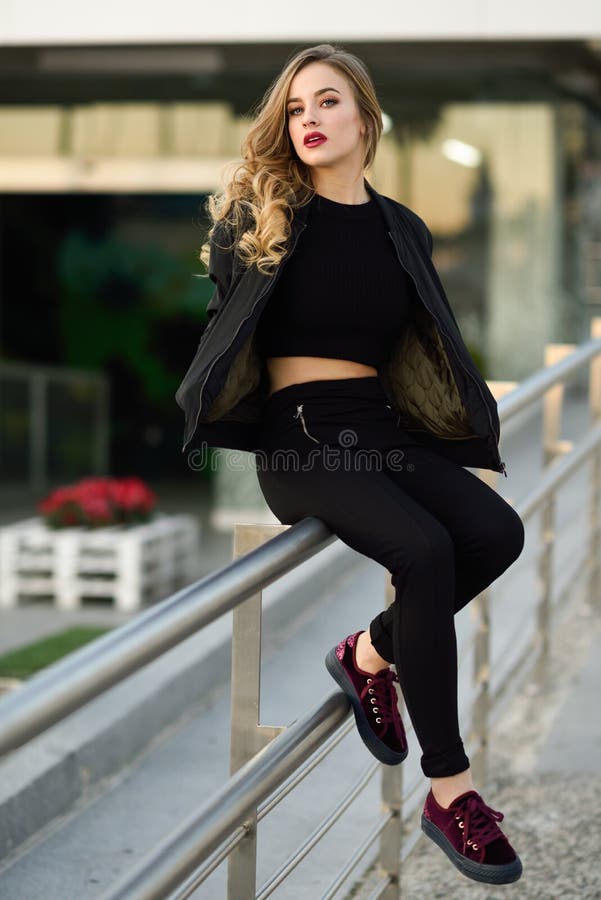 Beautiful young girl wearing black jacket sitting in the street.