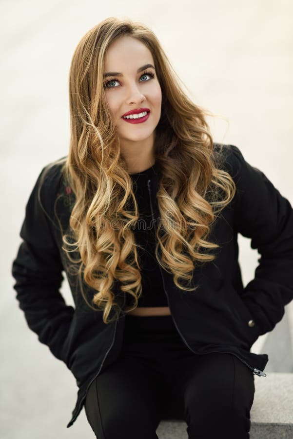 Beautiful young girl wearing black jacket sitting in the street.