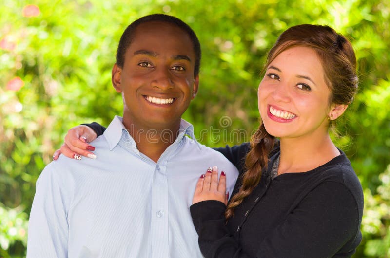 Beautiful Young Interracial Couple In Garden Environment Embracing And Smiling Happily To