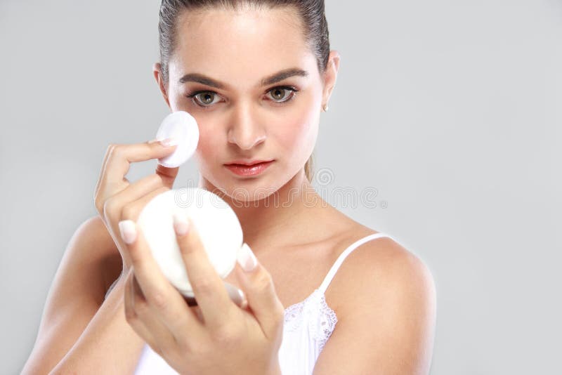 Beautiful young model holding a compact powder and applying some