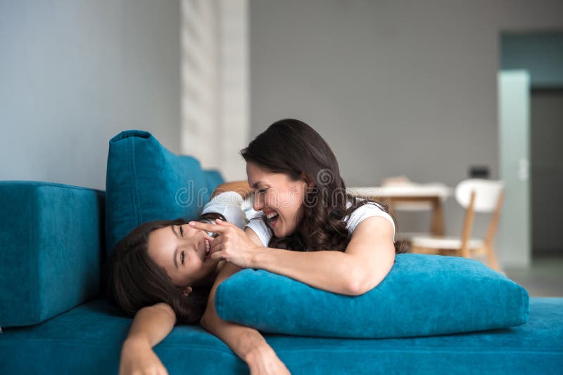 Beautiful young mother and her cute teen daughter having fun on the sofa both smiling and grimacing royalty free stock photography Beautiful young mother and her cute teen daughter having fun on the sofa both smiling and grimacing royalty free stock photography
