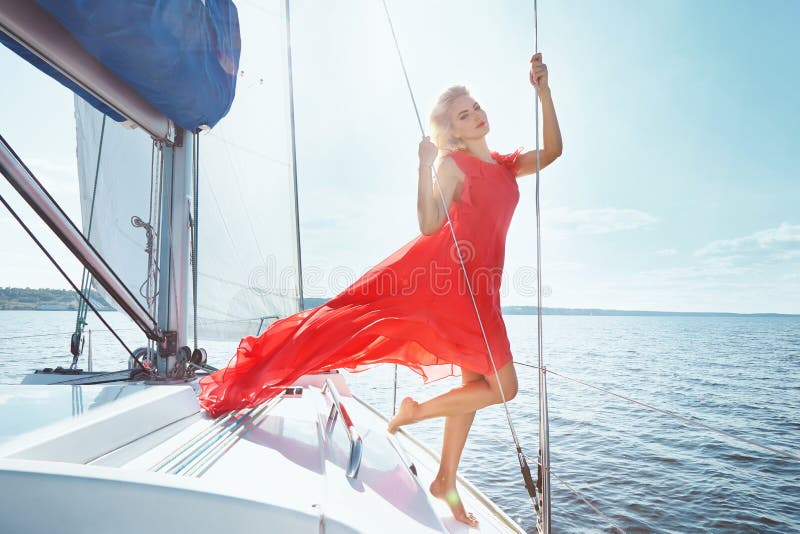 Beautiful young brunette girl in a dress and makeup, summer trip on a yacht with white sails on the sea or ocean in the Gulf