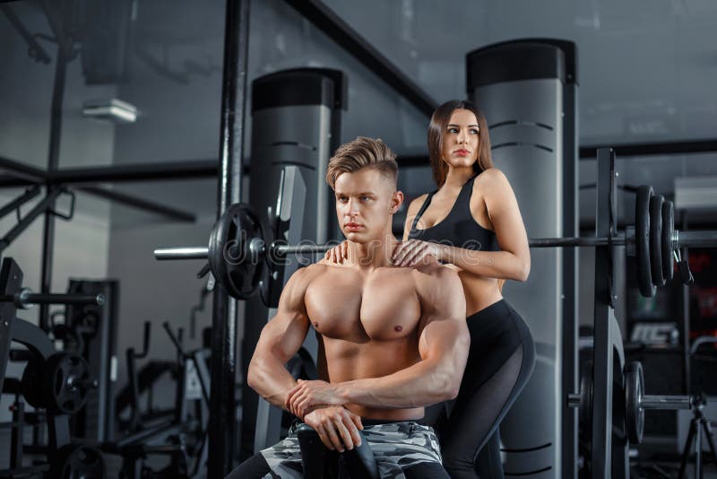 Beautiful young sporty couple showing muscle and workout in gym during phot...