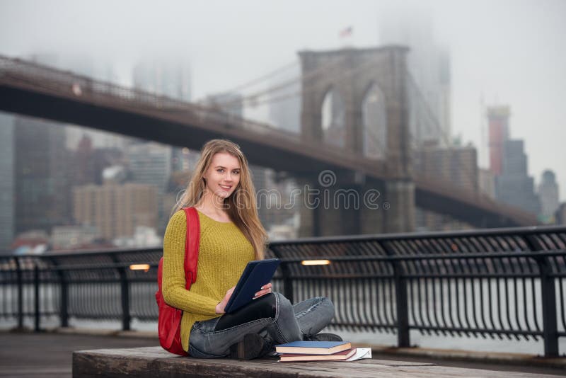 Beautiful young student girl using tablet pc outdoors in the city and study