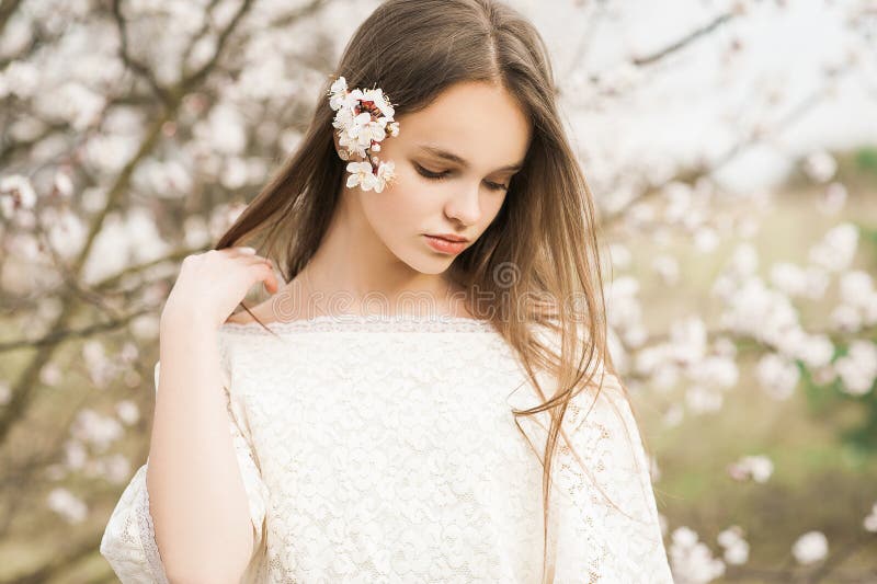 Beautiful young tender girl in blossom garden on a spring day, flower petals falling from the tree, closed her eyes and holding a