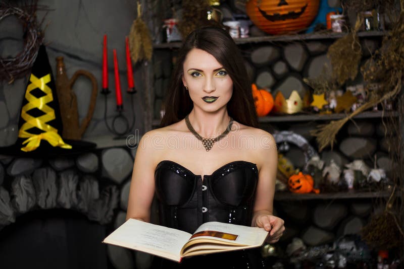 witch in a black corset with a book in his hands conjures reads a spell. Girl in costume on halloween