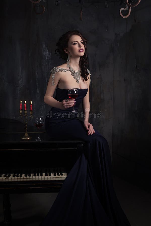 Beautiful young woman in black dress next to a piano with candelabra candles and wine, dark dramatic atmosphere of the castle. stock photo Beautiful young woman in black dress next to a piano with candelabra candles and wine, dark dramatic atmosphere of the castle. stock photo