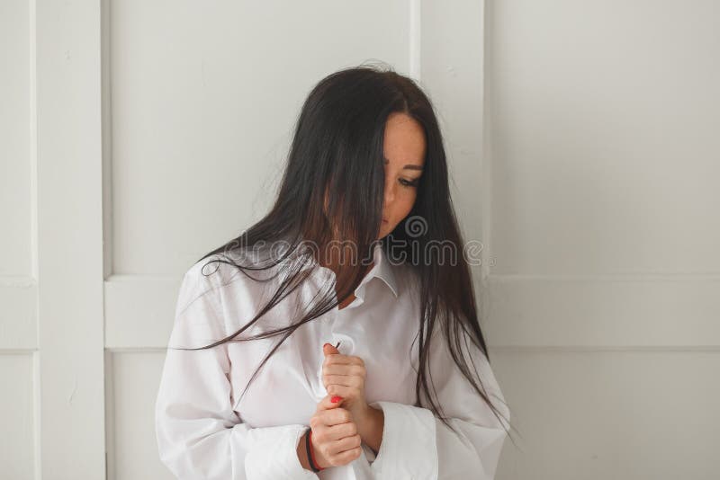 Beautiful young woman buttoning her shirt while dressing or undressing as she changes her or thinking