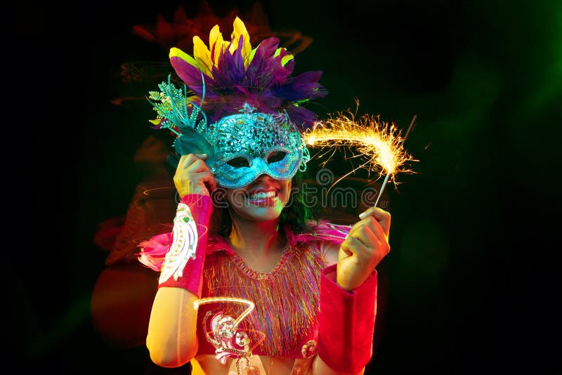 Beautiful young woman in carnival mask and masquerade costume in colorful lights