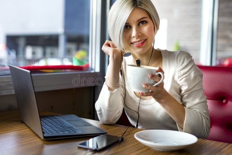 Portrait of beautiful young woman holding coffee cup with laptop and smartphone on table in cafe. Portrait of beautiful young woman holding coffee cup with laptop and smartphone on table in cafe