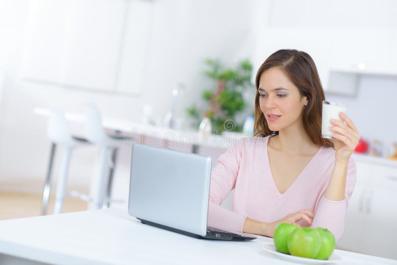 Beautiful young woman with coffee using laptop in the kitchen