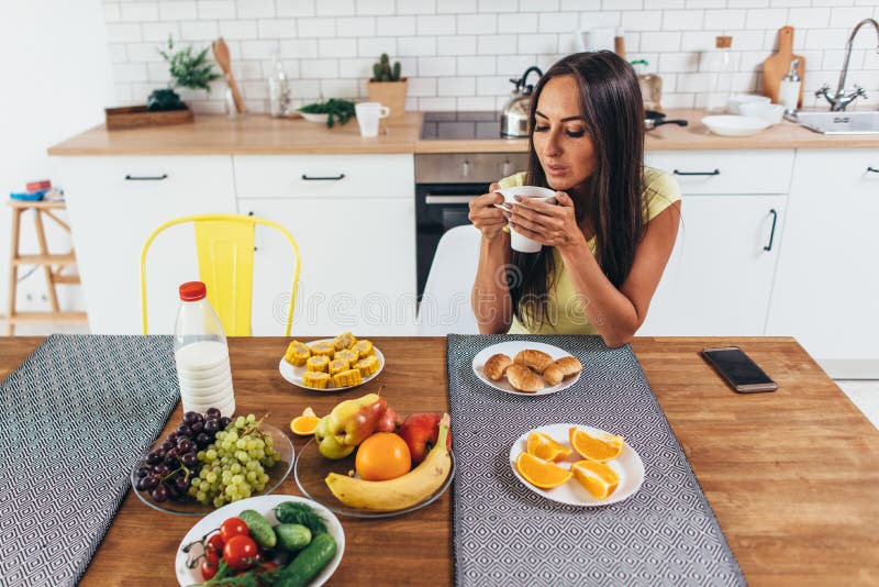 Beautiful young woman with a cup of coffee at home against kitchen background stock photo Beautiful young woman with a cup of coffee at home against kitchen background stock photo