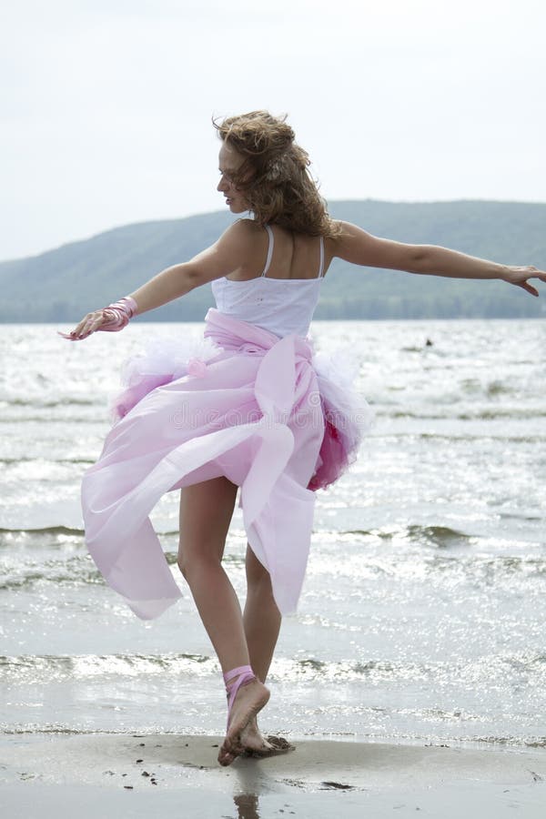 The beautiful young woman dances on a beach