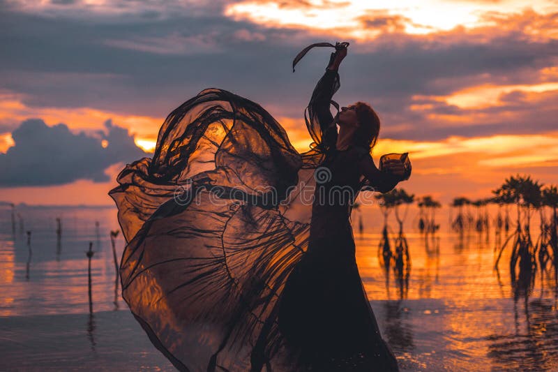 Beautiful young woman dancing in water at sunset silhouette