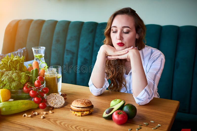 Beautiful Young Woman Decides Eating Hamburger or Vegetables in Kitchen ...