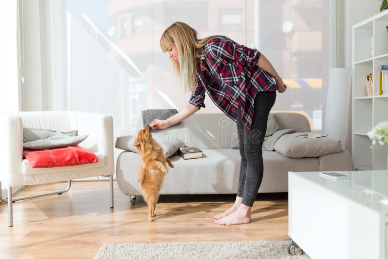 Beautiful young woman with dog playing at home.