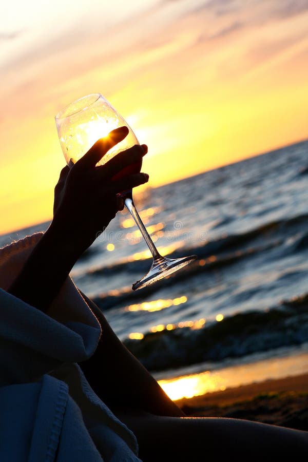 Beautiful young woman drinking wine on beach