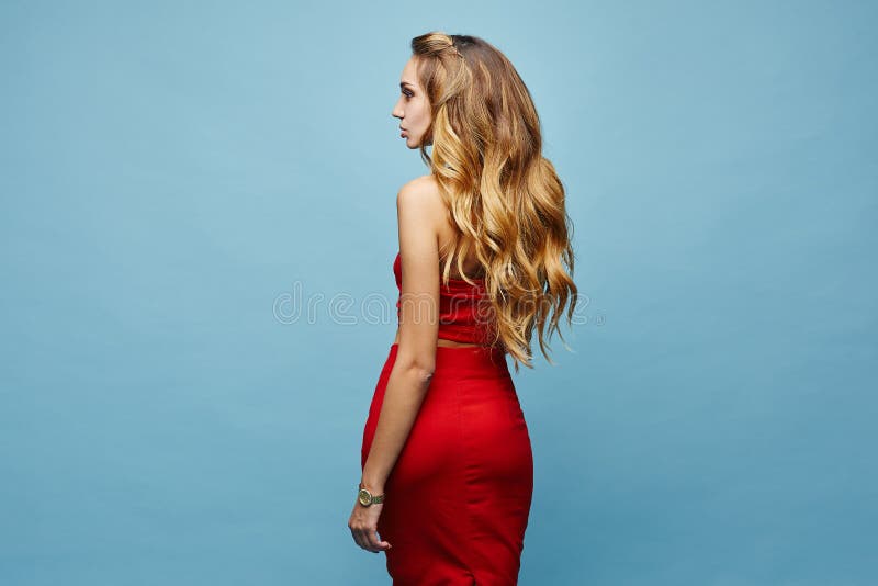 Beautiful young woman in elegant red outfit isolated at a blue background. Blonde model girl with perfect body in red