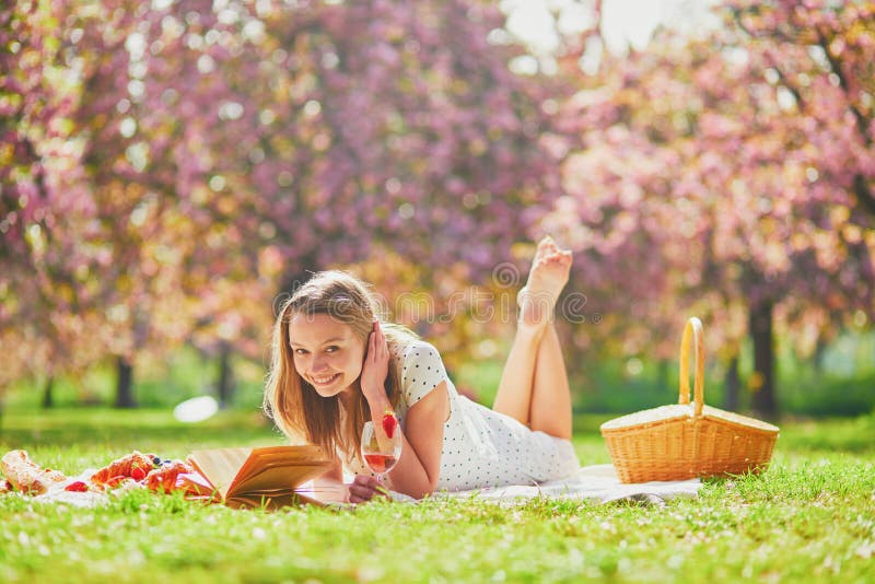Woman having picnic on sunny spring day in park during cherry blossom season stock photo Woman having picnic on sunny spring day in park during cherry blossom season stock photo
