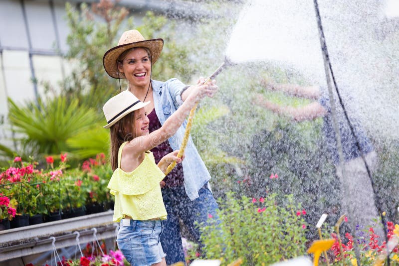 Beautiful young woman with her daughter watering the plants with a hose in the greenhouse.