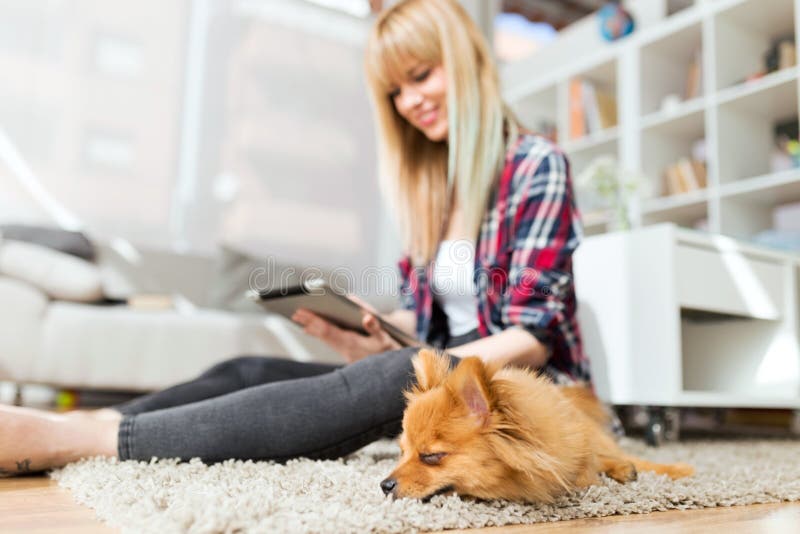 Beautiful young woman with her dog using digital tablet at home.