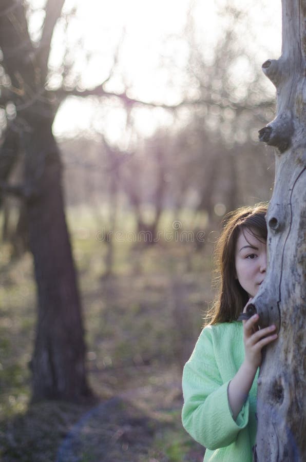 Beautiful young woman hiding behind a tree