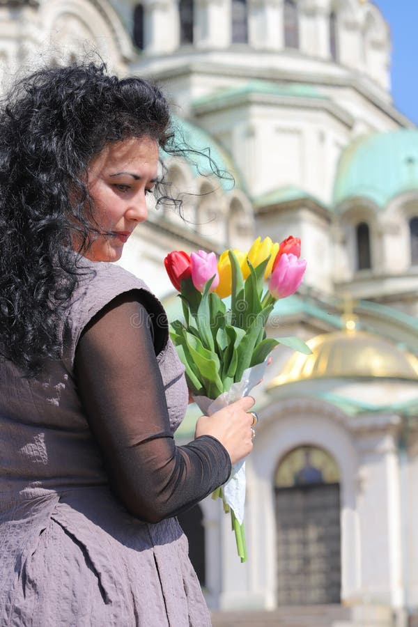 A beautiful young woman holding a bouquet of colorful tulips in front of the Alexander Nevsky Cathedral