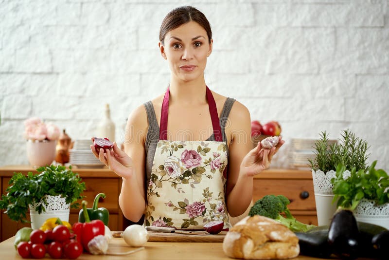 Beautiful young woman holds onions and garlic in the kitchen at a table full of organic vegetables