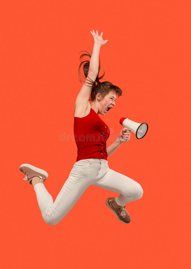Beautiful young woman jumping with megaphone isolated over red background stock image Beautiful young woman jumping with megaphone isolated over red background stock image