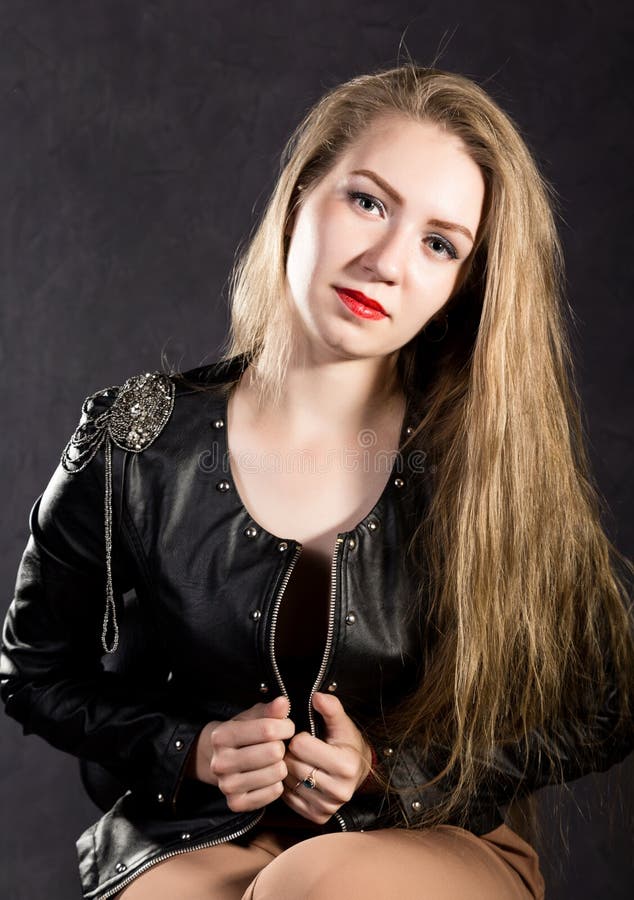 Beautiful young woman in a leather jacket posing on a gray background