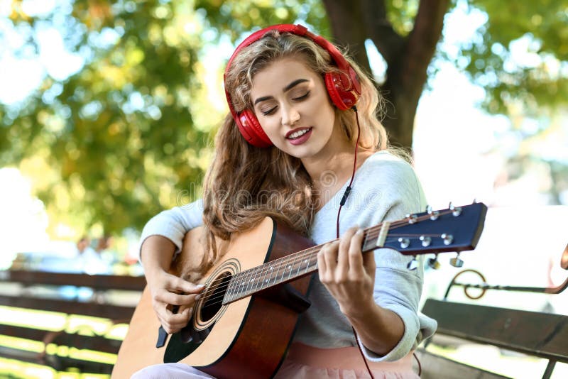 Beautiful young woman listening to music and playing guitar in park