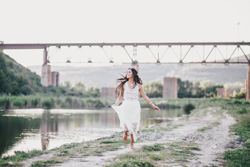 Beautiful young woman with long curly hair dressed in boho style dress posing near lake