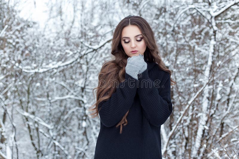 Beautiful young woman with long dark hair sad lonely walk in the winter woods in a black jacket and mittens