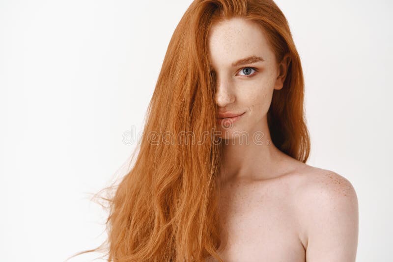 Beautiful young woman with long perfect red hair and blue eyes looking at camera, standing naked, showing pale clean