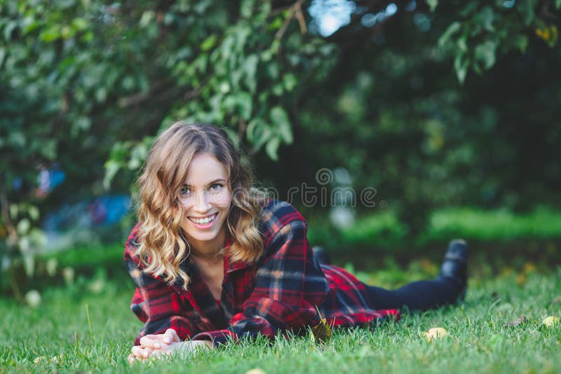 Beautiful young woman in a male flannel shirt lying on green grass