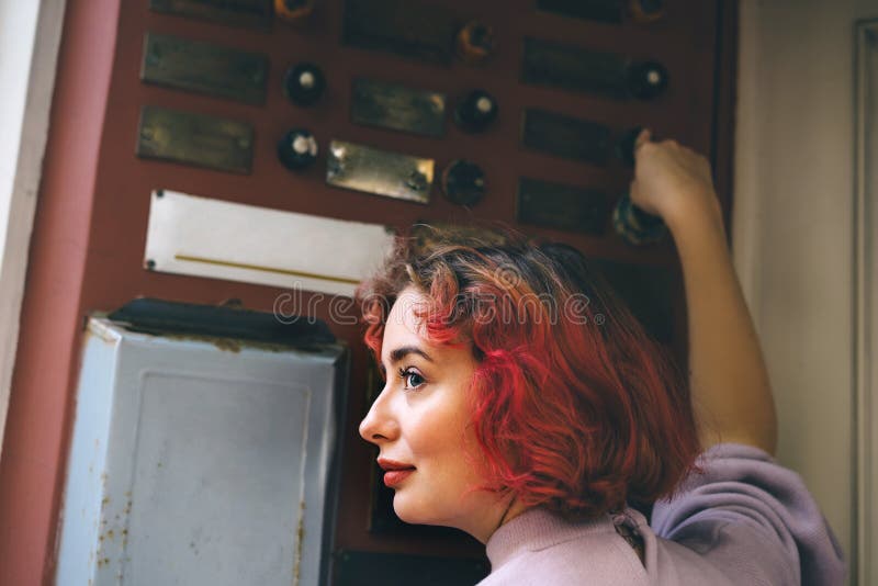 Beautiful young woman with orange hair ringing the door of an apartment royalty free stock photography Beautiful young woman with orange hair ringing the door of an apartment royalty free stock photography