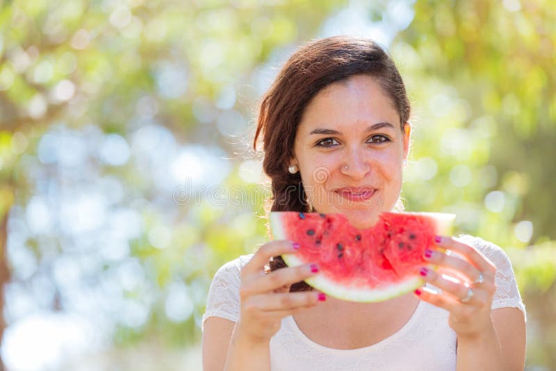 Beautiful young woman at park eating a slice of watermelon