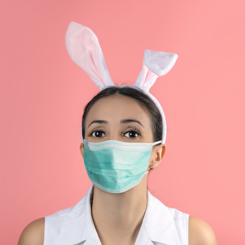Beautiful young woman with pink bunny ears and medical mask on pink background. Minimal Easter concept royalty free stock photography