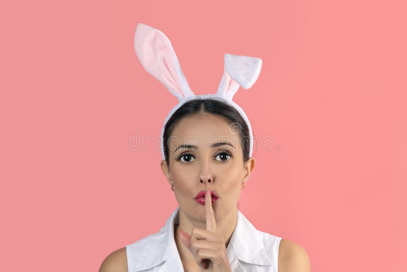 Beautiful young woman with pink bunny ears showing silence gesture on pink background. Minimal Easter concept royalty free stock image