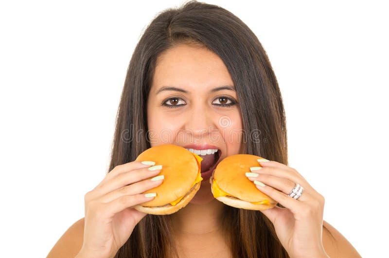 Beautiful young woman posing for camera holding two hamburgers next to mouth, smiling happily, white studio background stock image