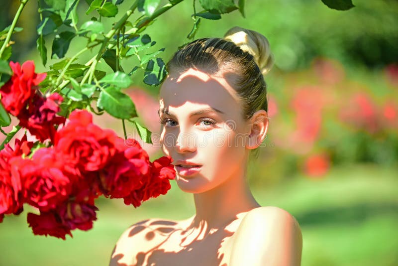 Beautiful young woman posing near roses in a summer garden. Girl in walking in the garden, red roses.