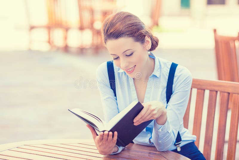 Beautiful young woman reading book outdoors. Positive face expression