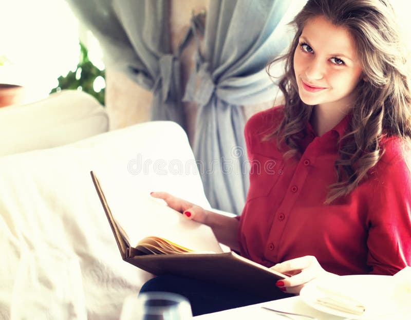 Beautiful young woman reading menu while sitting at the restaurant or cafe stock image