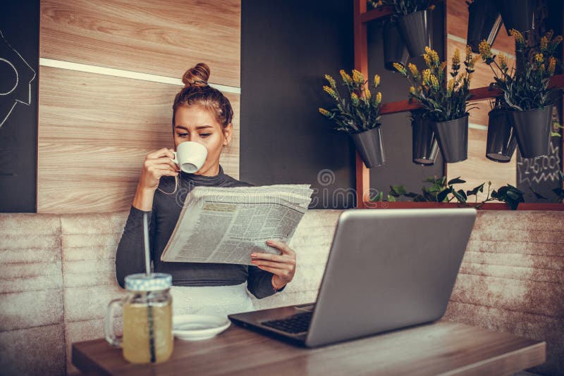 Beautiful young woman reading newspaper and drinking coffee in