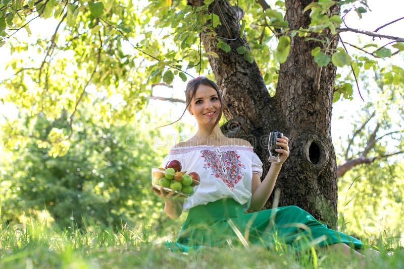 Beautiful young woman sitting under a tree with a plate of fruit and a glass of energii