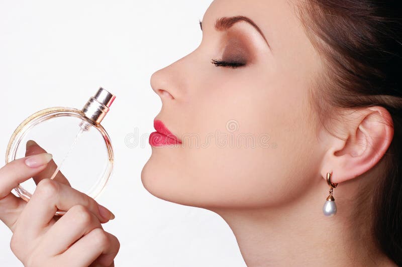 Beautiful young woman smelling her perfume isolated