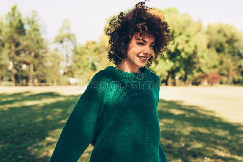 Beautiful young woman smiling posing against nature background with windy curly hair, have positive expression, wearing in green