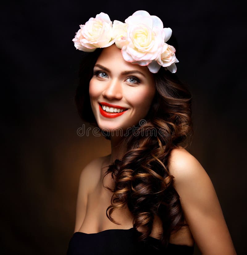 Beautiful Young Woman with Summer Pink Flowers. Long Permed Curly Hair and Fashion Makeup. Beauty Girl with Flowers